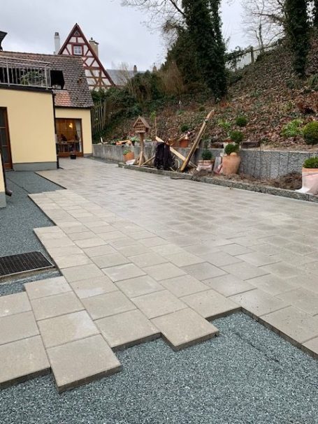 Pflasterarbeiten auf einer hellen Terrasse mit Pflanzen im Hintergrund.