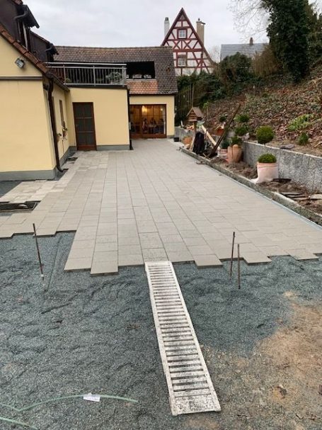 Blick auf eine neu verlegte Terrasse mit Platten und einem kleinen Holzsteg.