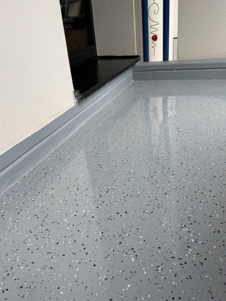 Glatte, graue Bodenfläche mit kleinen, dunklen Einsprengseln.