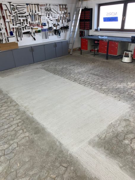 Werkstatt mit einem Teil neuem Betonboden und einem Bereich aus Pflastersteinen.