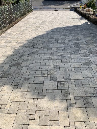 Gestreuter Pflasterweg mit Schatten und niedrigen Blumenrabatten entlang der Seite.