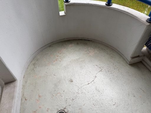 Runder Balkon mit hellem Boden und geländer, umgeben von grünem Gras.