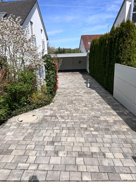 Pflasterweg zwischen weißen Häusern, umgeben von Frühlingsträuchen und Hecken.