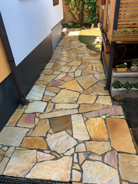 Ein gepflasterter Weg aus bunten Steinen, der durch einen Garten führt.