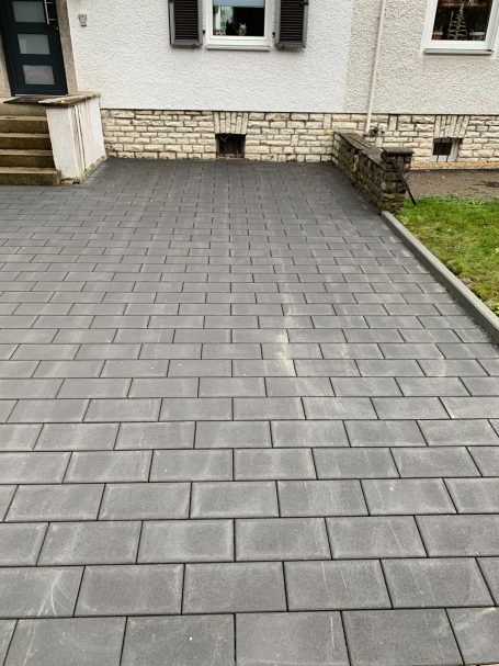 Gepflasterte Auffahrt vor einem Haus mit Fenster und Steinstufen.