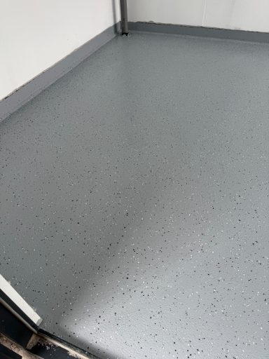 Grau gestrichener Boden mit leicht schimmernder Oberfläche und kleinen Farbsprenkeln.