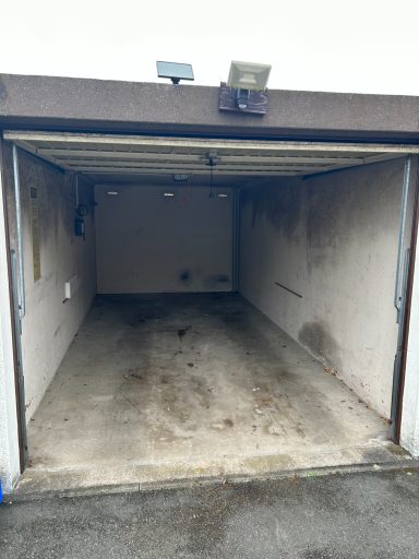 Leerer Garagenraum mit grauen Wänden und verschmutztem Boden.