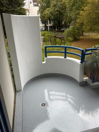 Balkon mit grauem Bodenbelag, blauer Brüstung und Blick auf einen Garten.
